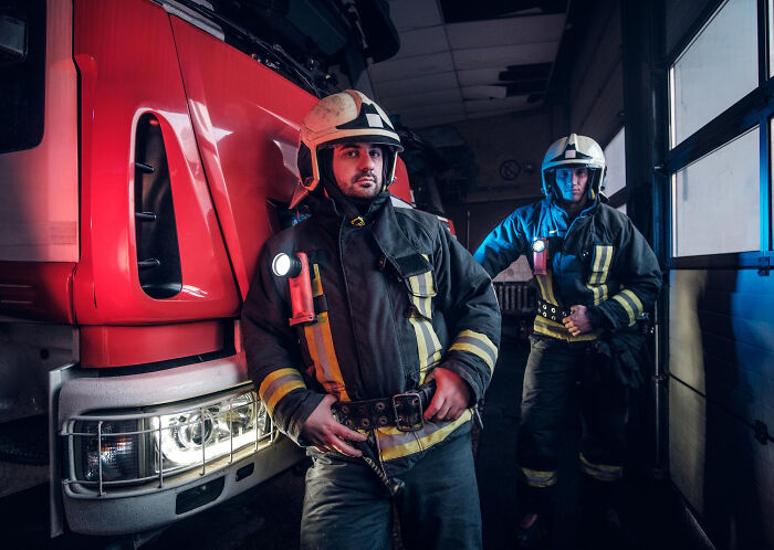 Two firefighters with helmets and flashlights in front of a fire truck, highlighting jobs that make women swipe left.