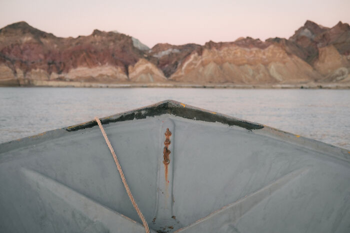 The bow of a small boat on the Strait of Hormuz, with colorful mountains in the background, showcasing the geopolitical hotspot.