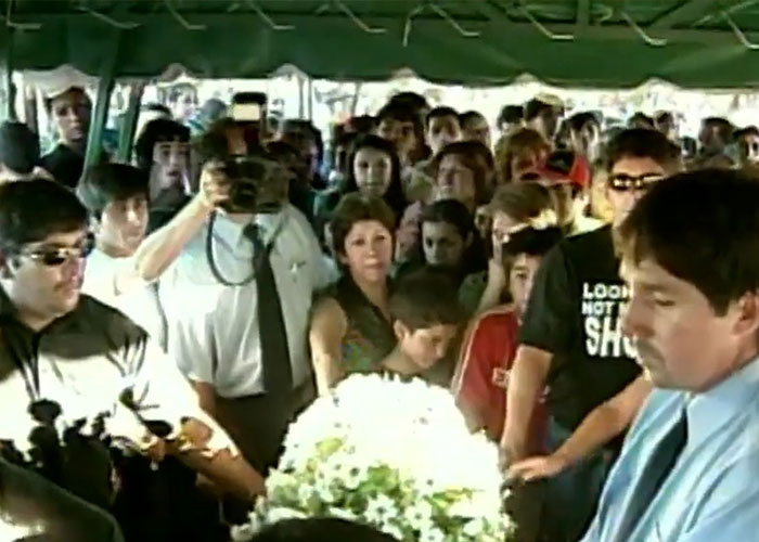 Mourners surrounding a flower-covered casket, a somber moment for the disappeared man.