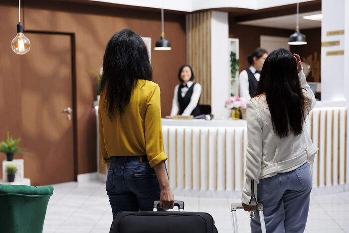 Two women with luggage approaching a hotel reception desk, a scene reflecting why people got fired from their jobs.