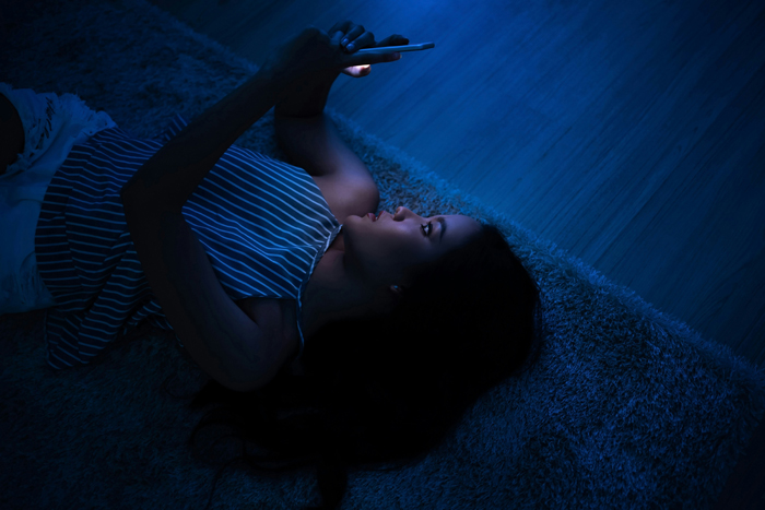 A young woman lies in the dark, illuminated by her phone, experiencing creepy and mysterious things.