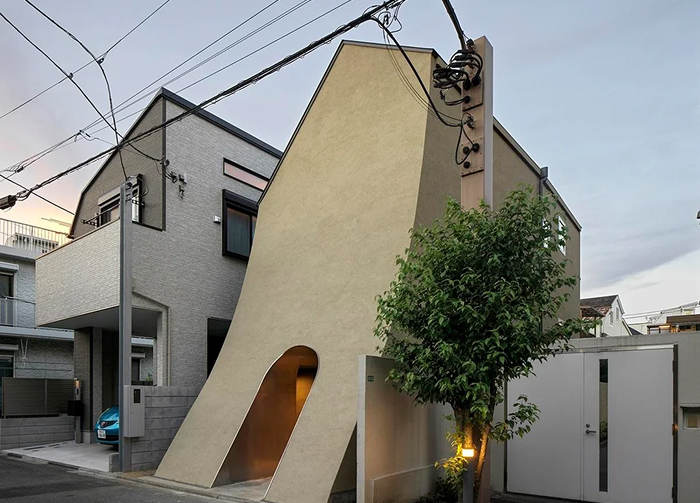 Unique modern architecture design with an angled, cream-colored wall forming an entryway, next to a residential building.