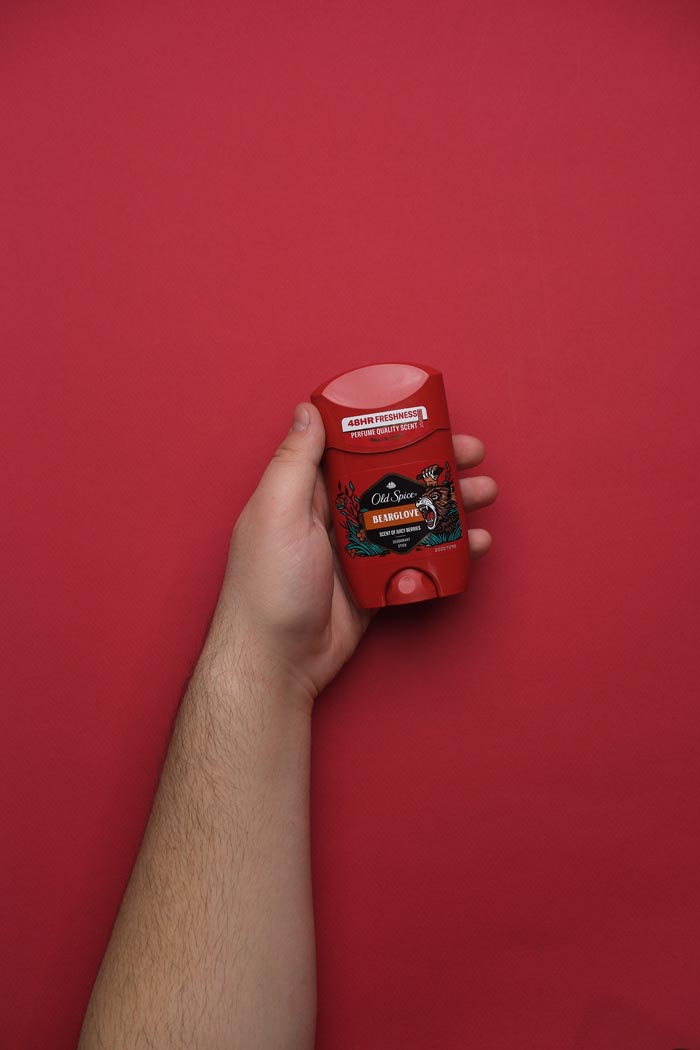 A hand holding Old Spice Bearglove deodorant, contrasting with unhygienic situations.