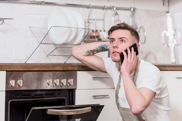 A man talks on the phone, looking concerned in a kitchen, reflecting on dumb reasons people got fired.