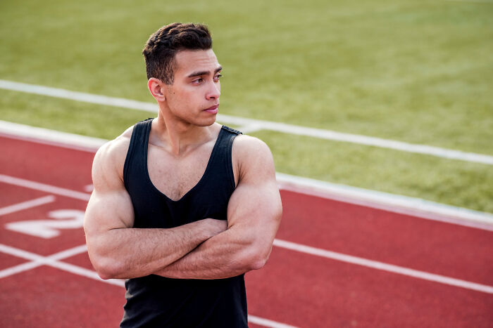 A muscular athlete in a black tank top on a running track, symbolizing jobs that make women swipe left.