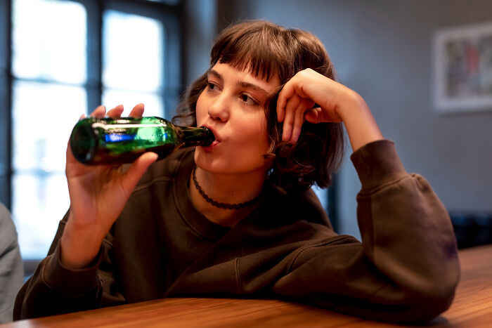 A young woman drinking from a green bottle, potentially after a bad pocket dial story, contemplating her lock screen.