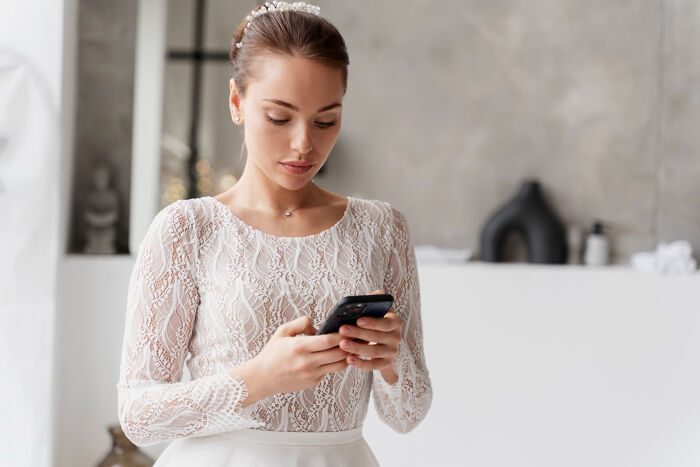 A bride in a white lace dress intently looking at her phone. One of the dumbest reasons people got fired.