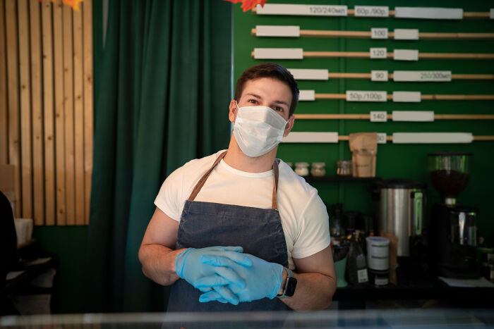 A man wearing a face mask and gloves stands behind a counter, representing reasons people got fired.