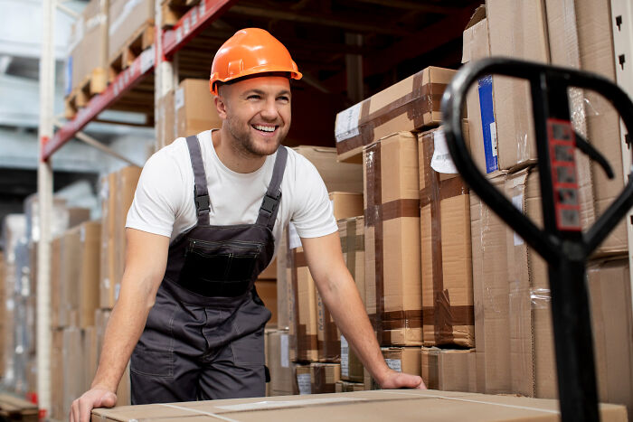 A happy warehouse worker pushes a pallet jack, thinking about dumb reasons people got fired.