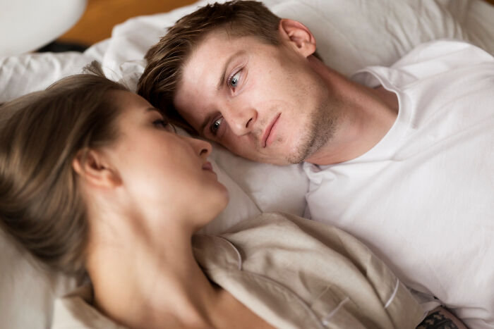 Couple lying in bed looking at each other, perhaps discussing embarrassing pocket dial stories.