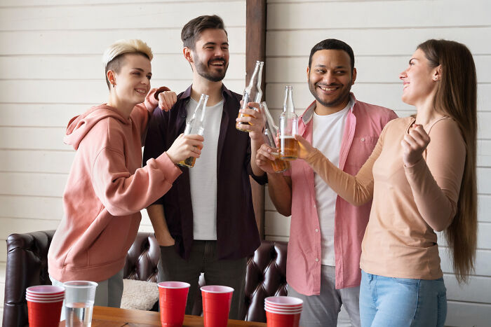 A group of friends laughing and drinking, enjoying a party, possibly leading to embarrassing pocket dial stories.