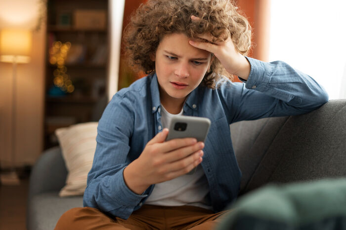 A young boy looking confused at his phone, illustrating a potentially bad pocket dial story and the importance of checking your lock screen.