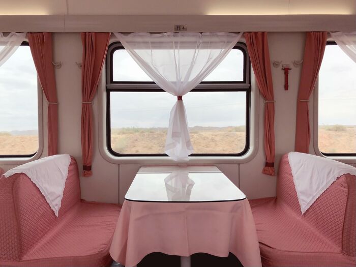 An empty train car interior with pink seating, white tablecloth, and desert view, a winning photo from the iPhone Photography Awards.
