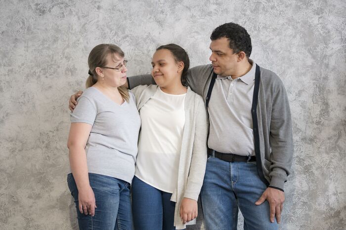 A couple and a teenage girl share an embrace, looking at each other, depicting an age-gap relationship.
