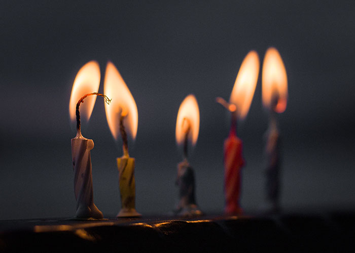 Five lit birthday candles of various colors, some still burning, reflecting the sentiment of no longer looking forward to birthdays.