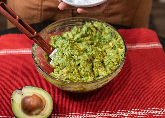 A person's hands holding a bowl of freshly mashed guacamole with an avocado half nearby, a simple comfort for difficult birthdays.
