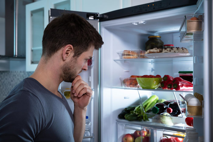 Man looks inside a fridge, contemplating the food choices. The image highlights the theme of raiding food and locking the fridge.