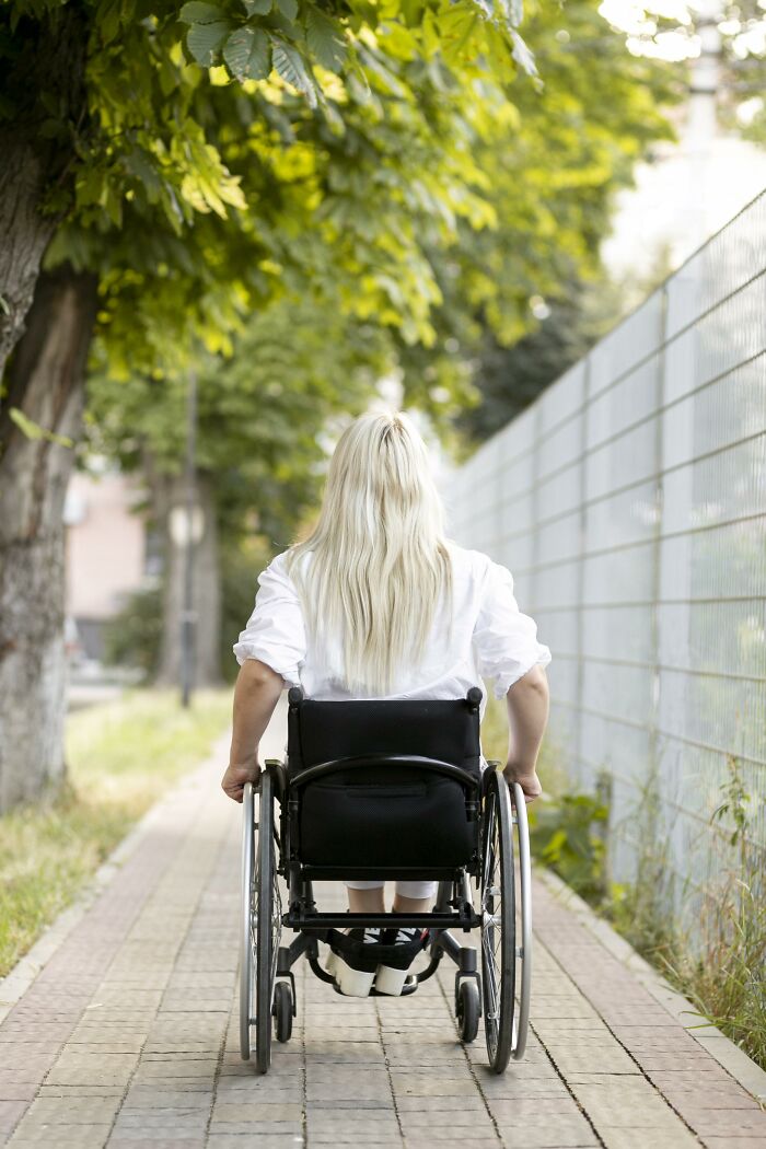 A woman with blonde hair in a wheelchair, seen from behind, on a paved path, relating to age-gap relationships.