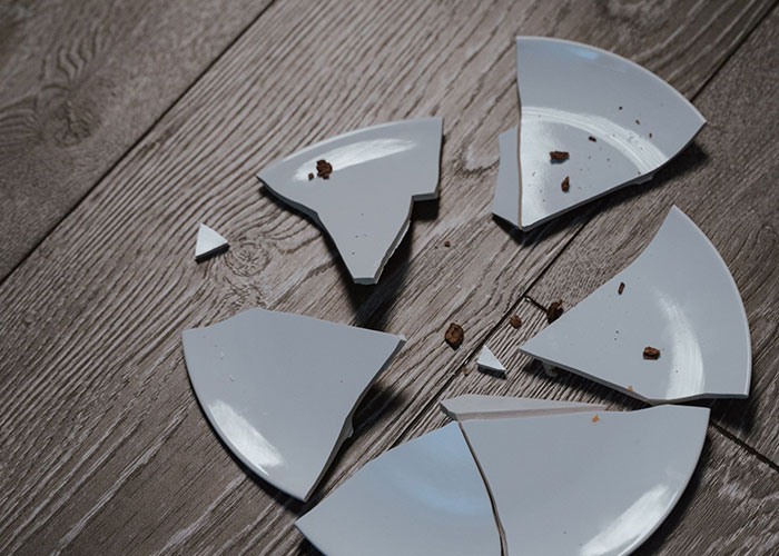 A broken white plate shattered into pieces on a wooden floor, representing the loneliest time and sad birthdays.