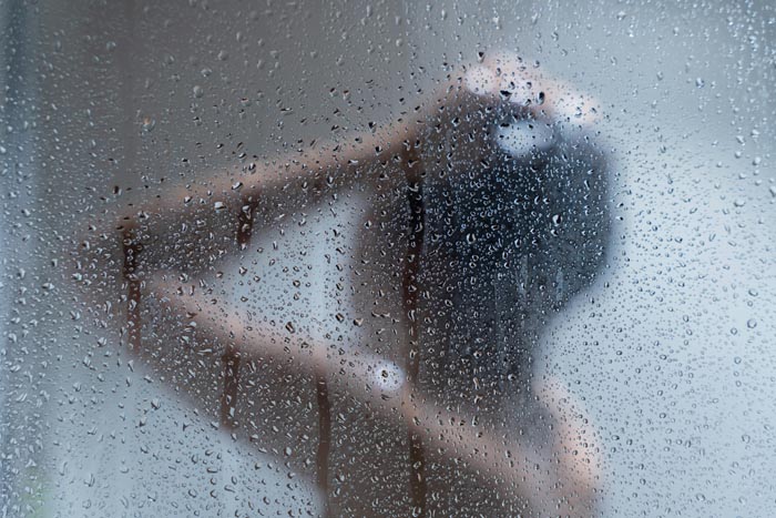 Person showering behind a wet glass door, emphasizing personal hygiene.