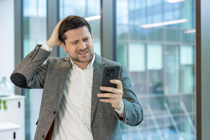 A man looking stressed while checking his phone, perhaps reacting to a bad pocket dial story or a lock screen issue.