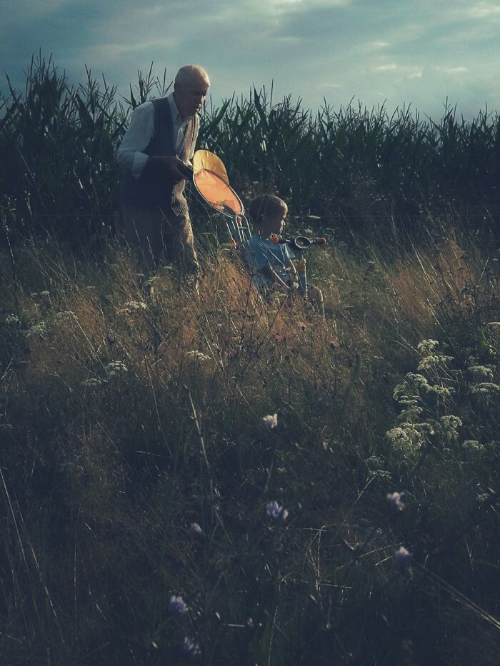 A man and a child in a field of tall grass with an orange paddle, an extraordinary winning photo for the iPhone Photography Awards.
