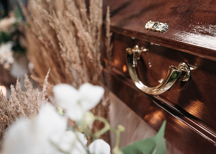 A dark wooden casket with ornate gold handles, surrounded by flowers, evoking the feeling of not looking forward to birthdays.