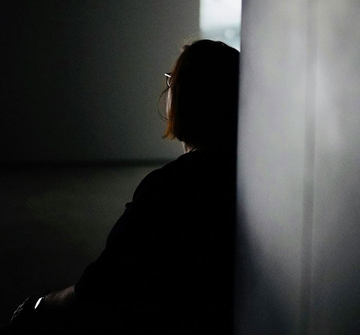 A woman sitting in a dark room, facing away, deep in thought. Hard truths women learned.