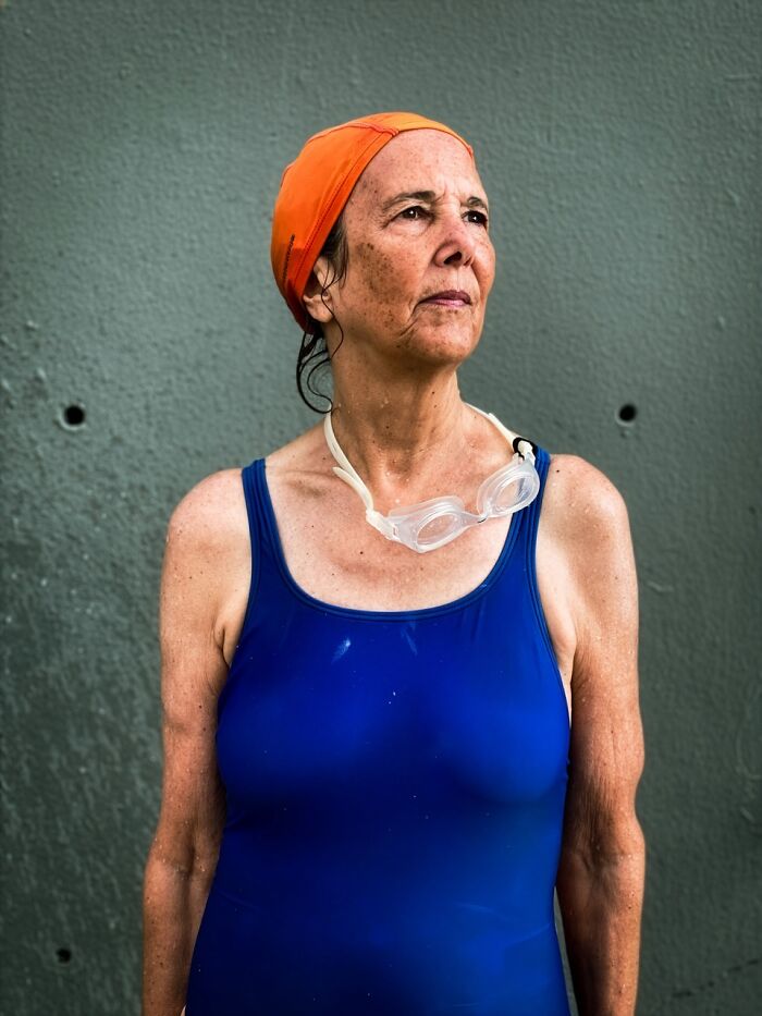 A woman in a blue swimsuit and orange swim cap with goggles around her neck, an extraordinary winning photo from the iPhone Photography Awards.