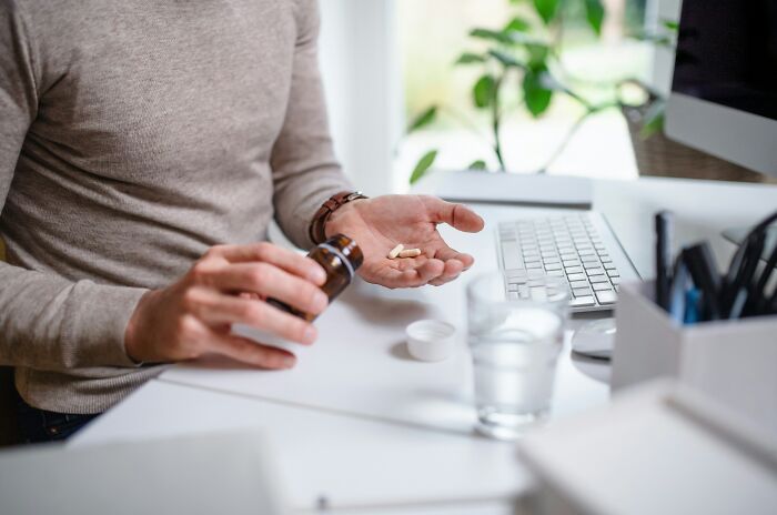 A man pouring pills into his hand at a desk, illustrating why people got fired from their jobs.