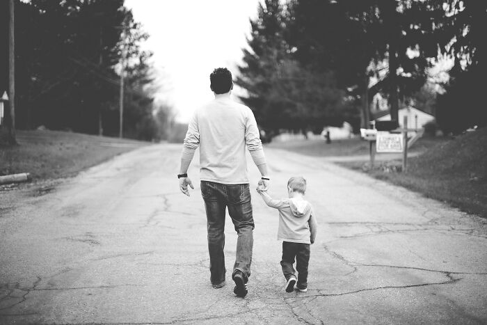 A father and young kid walking hand-in-hand down a road, seen from behind, depicting parents and kids.