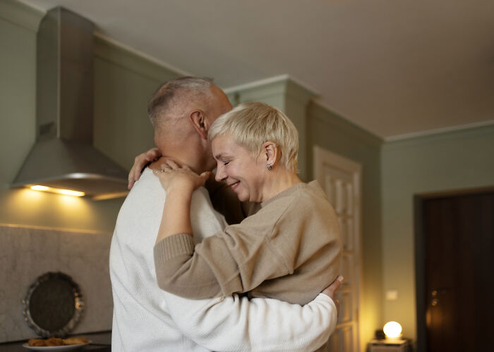 An older age-gap couple happily hugging in a kitchen, representing a successful relationship.
