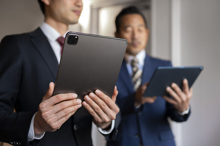 Two businessmen in suits look at tablets, a representation of professional environments where people got fired from their jobs.