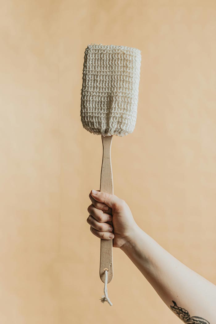 A hand holding a back scrubber, promoting good hygiene habits.