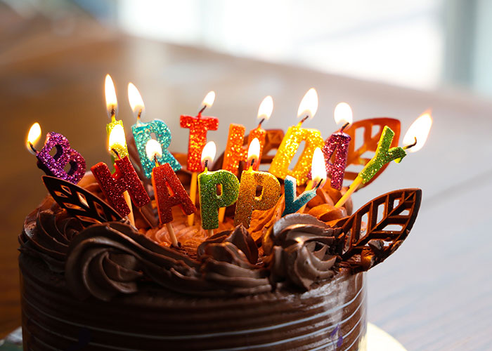 A chocolate birthday cake with lit candles spelling HAPPY BIRTHDAY, highlighting why some no longer look forward to their birthdays.