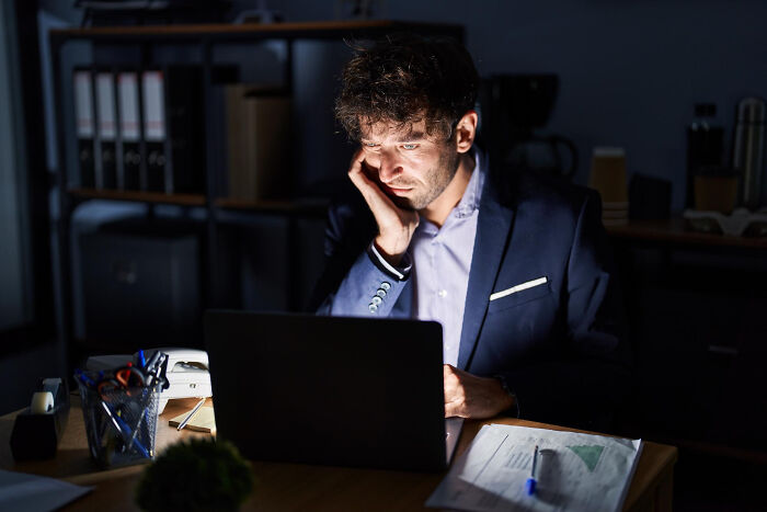 A man looking tired while working on his laptop late at night. One of the dumbest reasons people got fired.