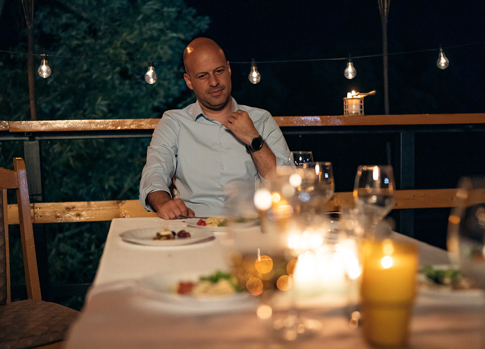A man in a light blue shirt sits at a candlelit table outdoors at night. An image related to wedding regrets.