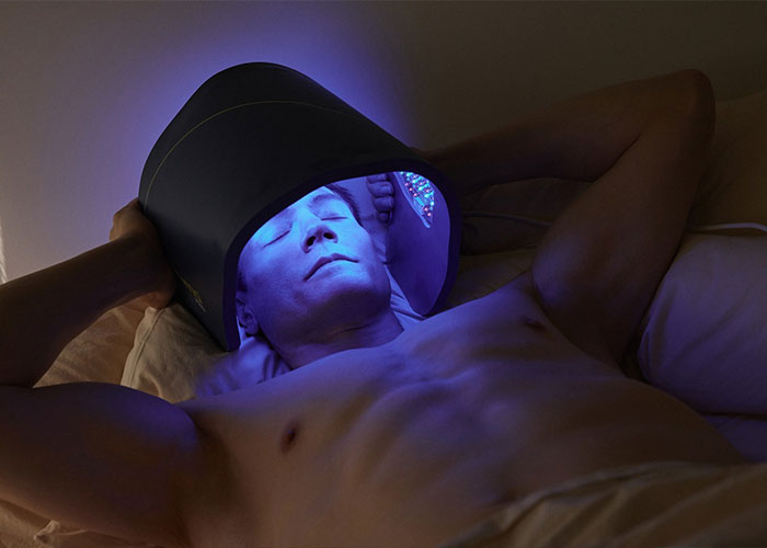 Biohacker Bryan Johnson using a futuristic light therapy device while lying down, showcasing his anti-aging biohacking routine. Biohacker Bryan Johnson using a futuristic light therapy device while lying down, showcasing his anti-aging biohacking routine.