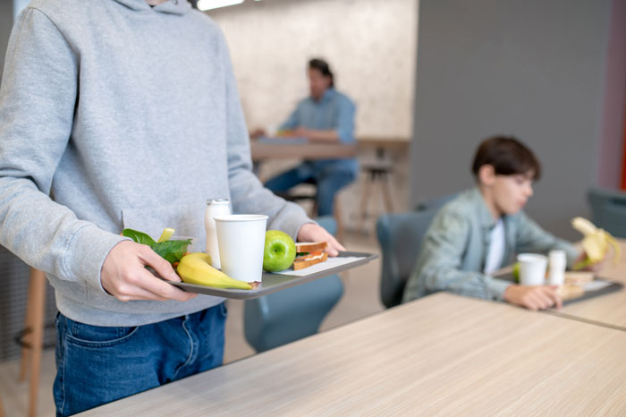 Teen shows friend forced to eat what she doesn't want at school cafeteria, carrying a tray of food. Teen shows friend forced to eat what she doesn't want at school cafeteria, carrying a tray of food.