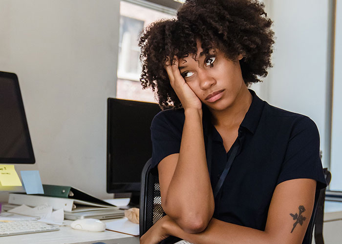 A woman with curly hair looking bored and resting her head on her hand, reflecting on her easy job and medium salary. A woman with curly hair looking bored and resting her head on her hand, reflecting on her easy job and medium salary.