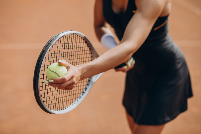 A woman prepares to serve a tennis ball, showing that sports can be surprisingly affordable.