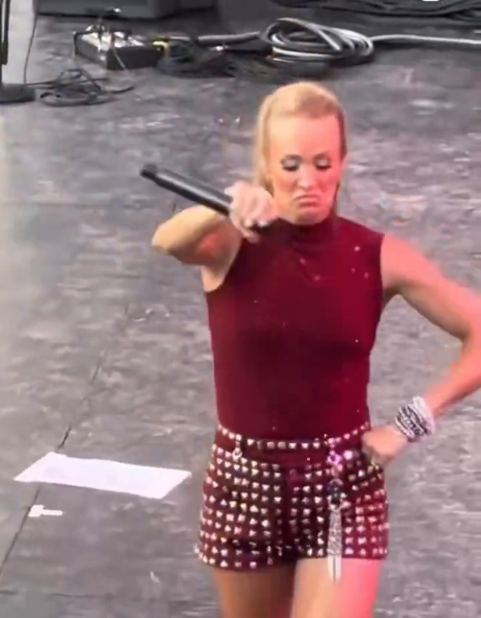 Carrie Underwood mid-performance, holding a microphone, subject to taunting for performance.