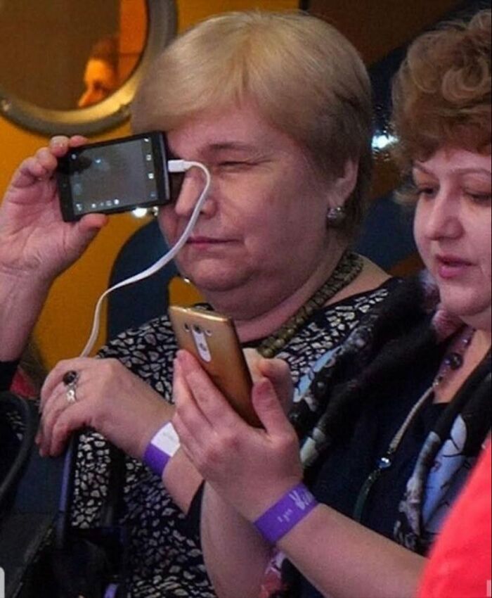 A woman holds a phone to her eye, humorously illustrating cultural decline into idiocy.