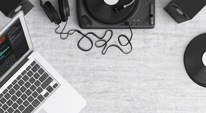 A laptop, turntable, headphones, and speakers on a table, symbolizing popular music taste and modern music consumption.