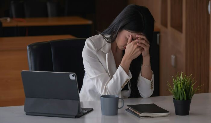 A stressed woman with her head in her hands at a desk, symbolizing why people got fired from their jobs.