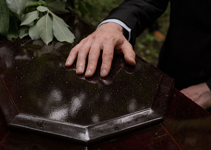 A man's hand rests on a coffin, reflecting on loneliness and no longer looking forward to birthdays.