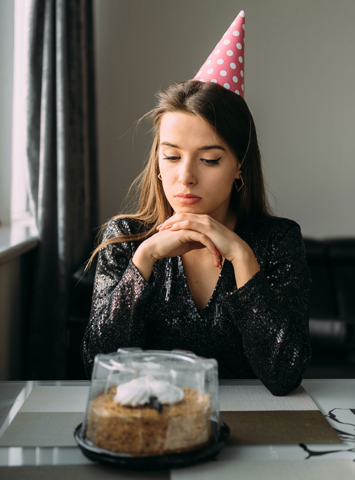A sad woman in a party hat looking at a cake, contemplating hard truths that women learned.
