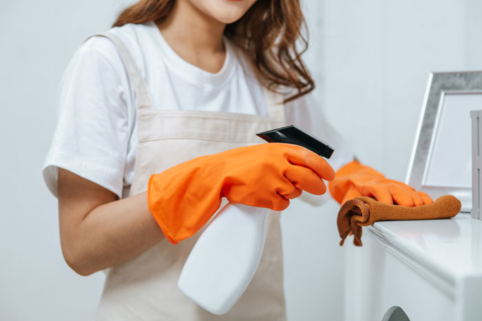 A person wearing orange gloves and cleaning a surface with a spray bottle, depicting domestic issues in partnerships.