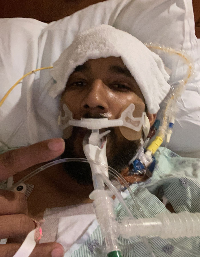 A man in a dire medical situation needing a transplant, lying in a hospital bed with medical tubes and a towel on his head.