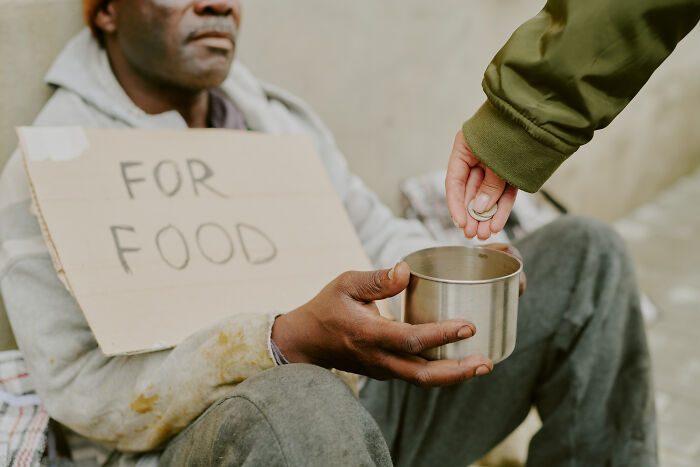 A person giving money to a homeless man holding a 'FOR FOOD' sign, representing kids questions that stumped parents.